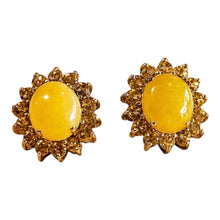 Load image into Gallery viewer, A pair of gold-toned stud earrings featuring oval yellow cabochon centers surrounded by a textured, petal-like halo of small clear stones, set against a plain white background.