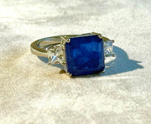 Load image into Gallery viewer, Ring with a blue gemstone and diamonds on a reflective surface