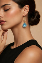Load image into Gallery viewer, Close-up of a woman wearing a blue teardrop earring against a beige background