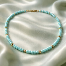 Load image into Gallery viewer, Turquoise beaded necklace with gold accents on a white fabric background