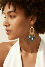 Load image into Gallery viewer, Woman wearing gold earrings with blue gemstones against a neutral background
