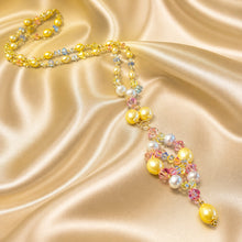 Load image into Gallery viewer, A luxury beaded necklace with yellow pearls, white pearls, and iridescent crystal clusters, displayed on a draped champagne satin fabric.
