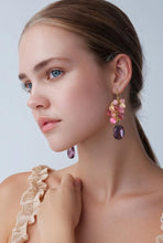 Load image into Gallery viewer, A close-up of a woman wearing a dangling earring with pink floral details and a purple teardrop gemstone, against a light gray background.