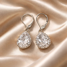 Load image into Gallery viewer, Pair of silver teardrop earrings with clear gemstones on a beige satin background