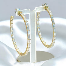 Load image into Gallery viewer, Gold hoop earrings with clear baguette crystals, displayed on a white jewelry stand against a soft white satin background.
