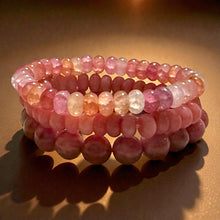 Load image into Gallery viewer, Stack of pink beaded  stretch bracelets on a reflective surface with a warm glow.
