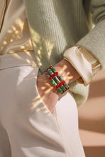 Load image into Gallery viewer, A close-up of a person wearing a stack of chunky beaded bracelets with alternating red and green cylindrical beads, styled with a cream satin shirt and a sage green knit sweater.
