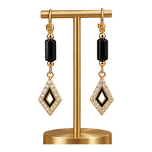 Load image into Gallery viewer, A pair of gold and black drop earrings with clear crystal pavé detailing, displayed on a gold jewelry stand against a white background.
