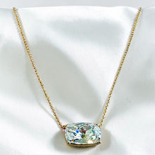 Load image into Gallery viewer, A gold chain necklace with a rectangular cushion-cut iridescent gemstone pendant, displayed on a white satin fabric background.
