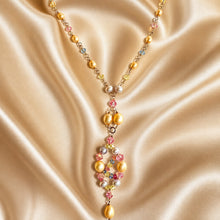 Load image into Gallery viewer, A luxury gold-toned necklace featuring yellow pearls, white pearls, and colorful faceted crystal beads in pink, blue, and yellow, displayed on a draped beige satin fabric.
