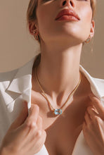 Load image into Gallery viewer, A close-up lifestyle shot of a model wearing a gold chain necklace with a light blue rectangular pendant, styled with gold hoop earrings and a white collared shirt.
