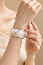 Load image into Gallery viewer, A close-up of a person's wrist wearing a chunky bracelet made of irregular, polished white quartz stones with subtle iridescent gold veining, set against a soft beige background.
