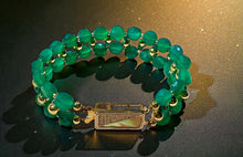 Load image into Gallery viewer, Green beaded bracelet with gold accents on a reflective surface
