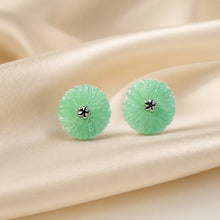 Load image into Gallery viewer, A pair of round light green jadeite stud earrings with a textured, scalloped edge and a small silver-toned flower center, displayed on draped cream satin fabric.
