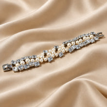 Load image into Gallery viewer, A silver-tone bracelet featuring rows of white pearls and clear crystals, displayed diagonally on a draped beige satin fabric background.
