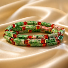 Load image into Gallery viewer, Three beaded stretch bracelets stacked together on a draped champagne satin fabric. The bracelets feature textured green stone beads, rectangular red faceted crystal spacers, and a central pink stone bead with white veining.
