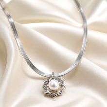 Load image into Gallery viewer, A silver snake chain necklace with a flower-shaped pendant holding a single white pearl, displayed on draped cream satin fabric.
