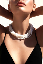 Load image into Gallery viewer, A close-up lifestyle shot of a model wearing a multi-strand white beaded collar necklace, styled with a black top under bright, direct sunlight.
