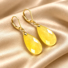 Load image into Gallery viewer, A pair of gold lever back drop earrings with faceted yellow jasper gemstone teardrop-shaped stones, displayed on a draped beige satin fabric background.
